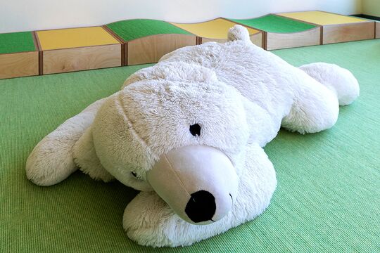 Ein weißer großer Teddybär liegt auf einem Teppich