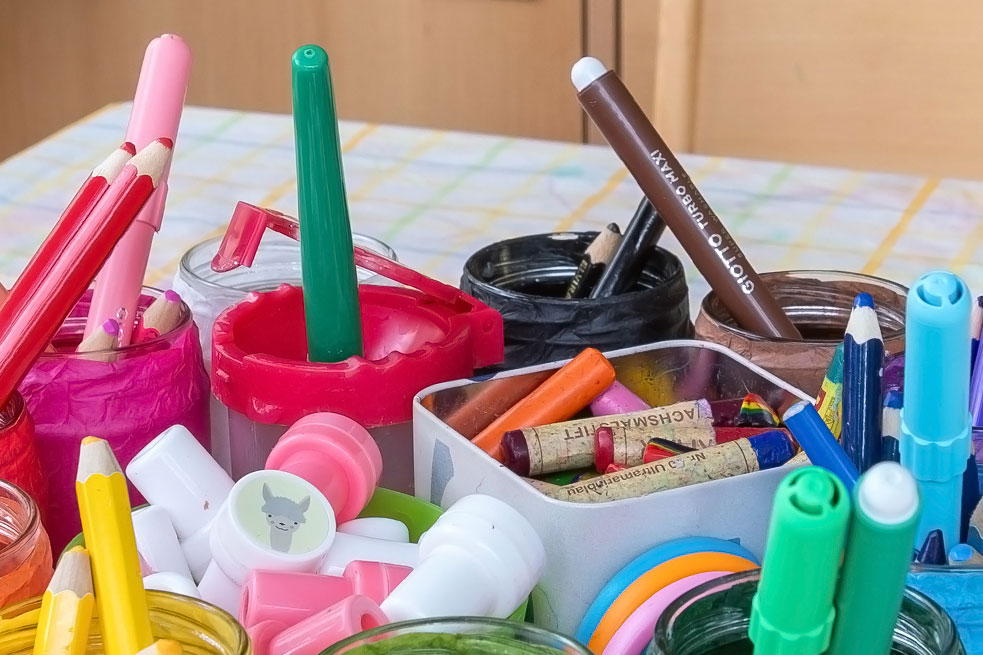 Becher und Dosen mit bunten Malstiften auf einem Tisch